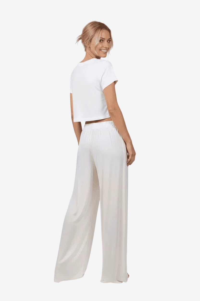 Donna indossa un pantalone palazzo color avorio in viscosa effetto raso dal taglio fluido.
