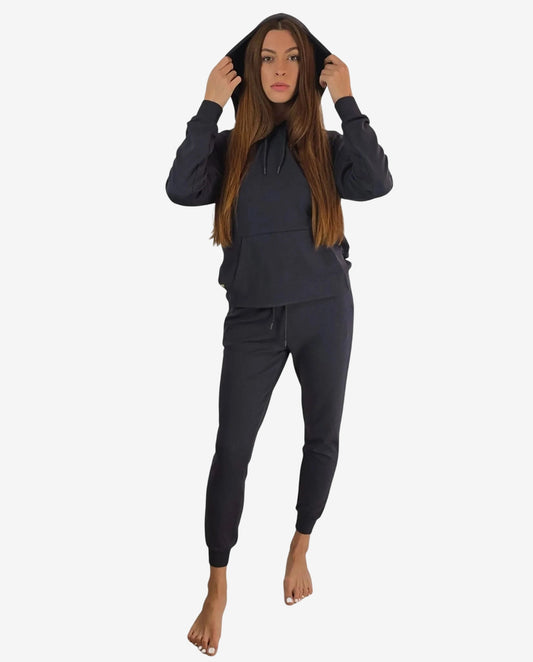 Modella che indossa una tuta sportiva nera con felpa a cappuccio e pantaloni jogger abbinati.