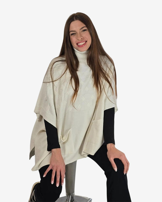 Donna che indossa un poncho color crema a collo alto sopra un maglione nero.