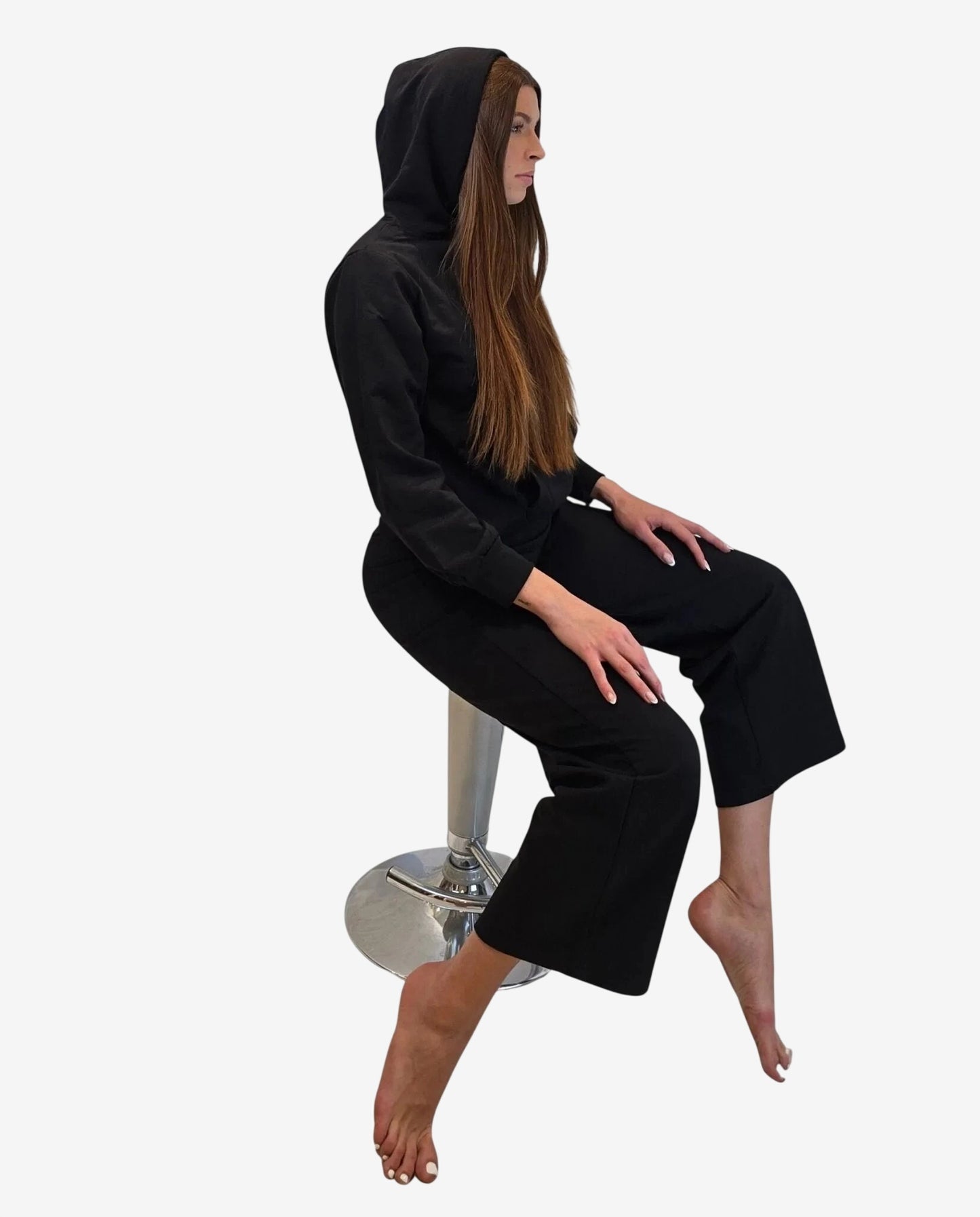 Modella seduta su uno sgabello indossa una felpa nera con cappuccio e pantaloni abbinati.