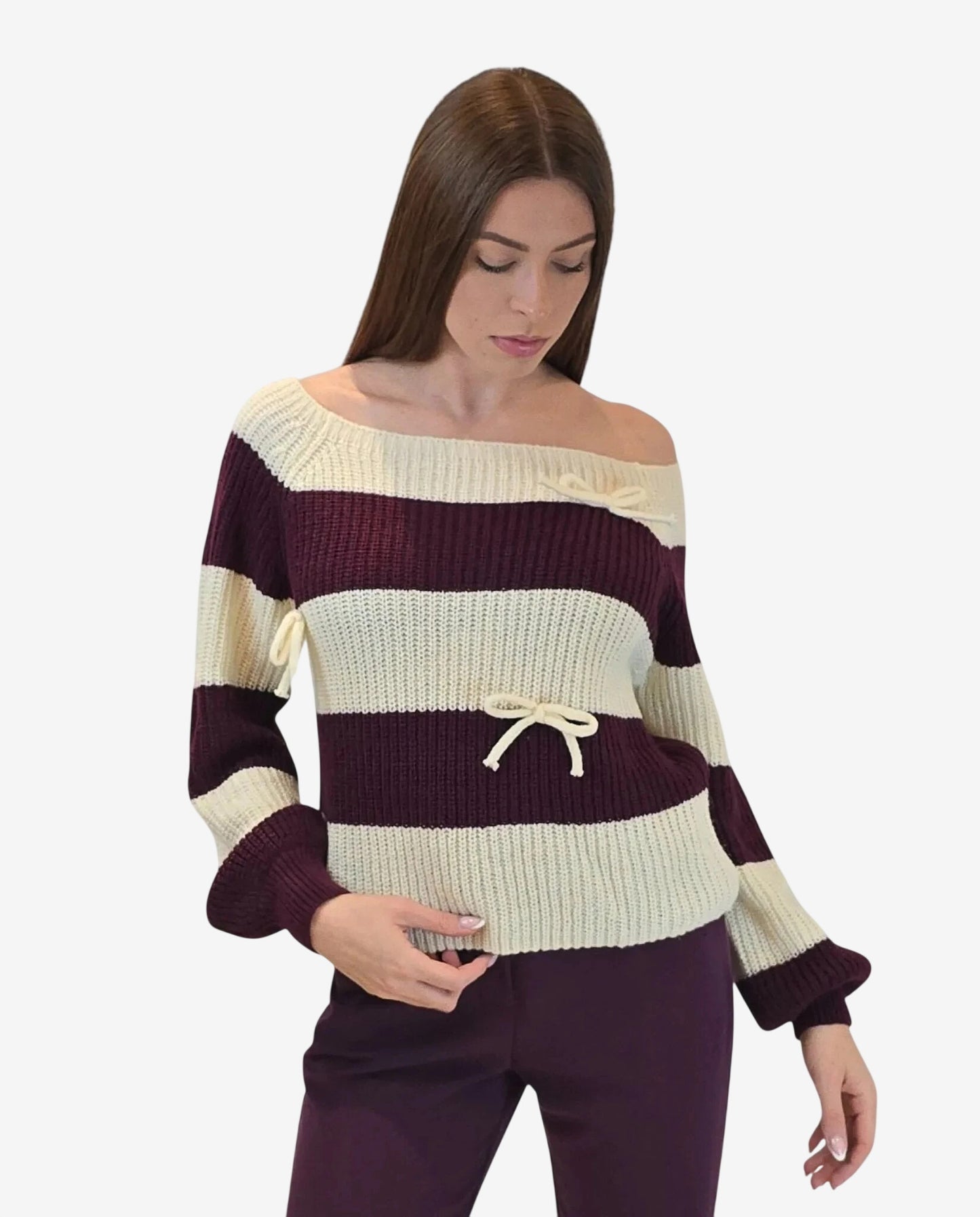 A woman wears a cream and burgundy striped off-the-shoulder sweater with decorative bow details.