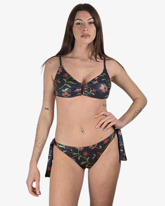 Modella che indossa un bikini a due pezzi in tessuto lurex scuro con stampa floreale colorata.