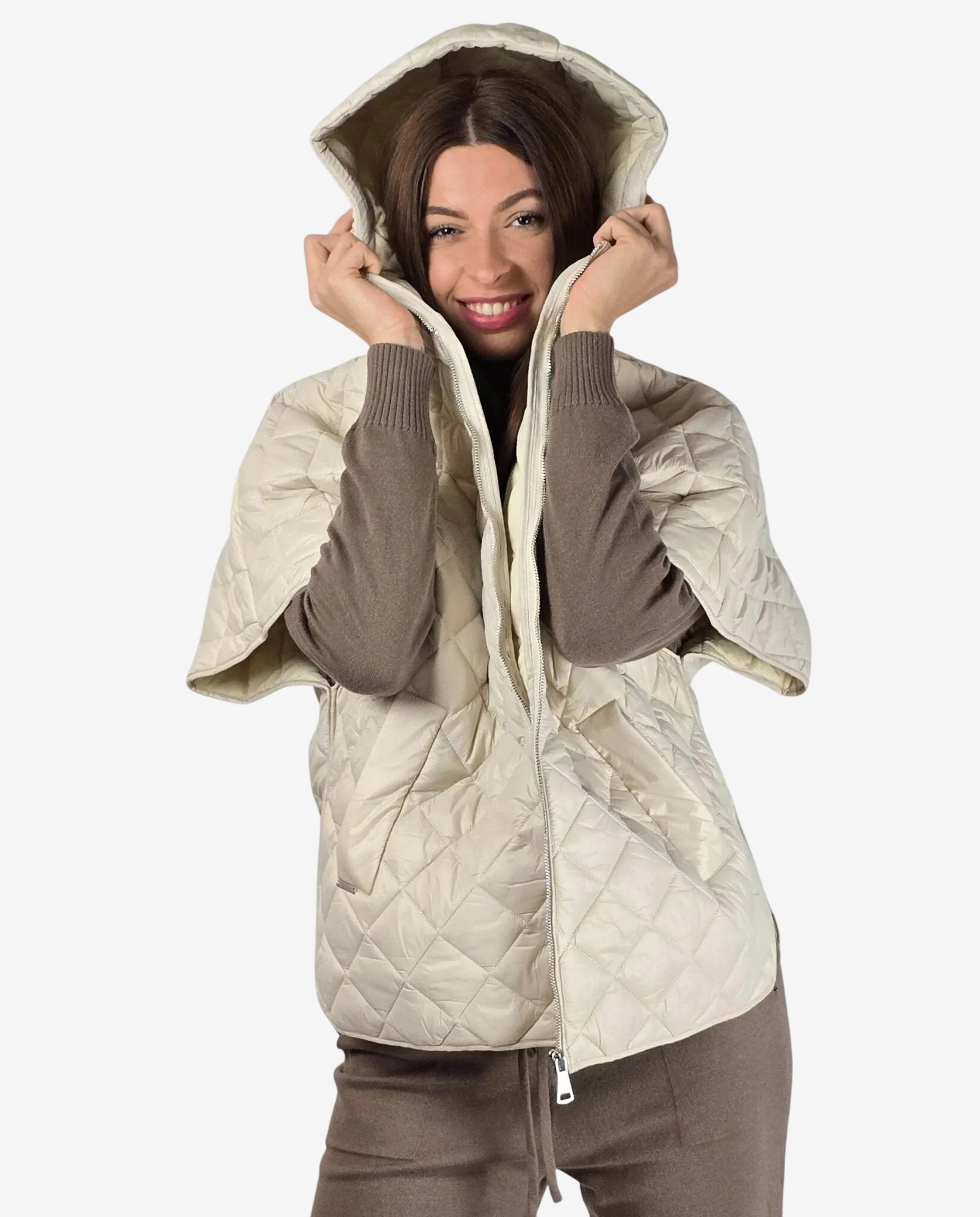 A woman wears a cream-colored quilted hooded vest with short sleeves over a brown sweater.