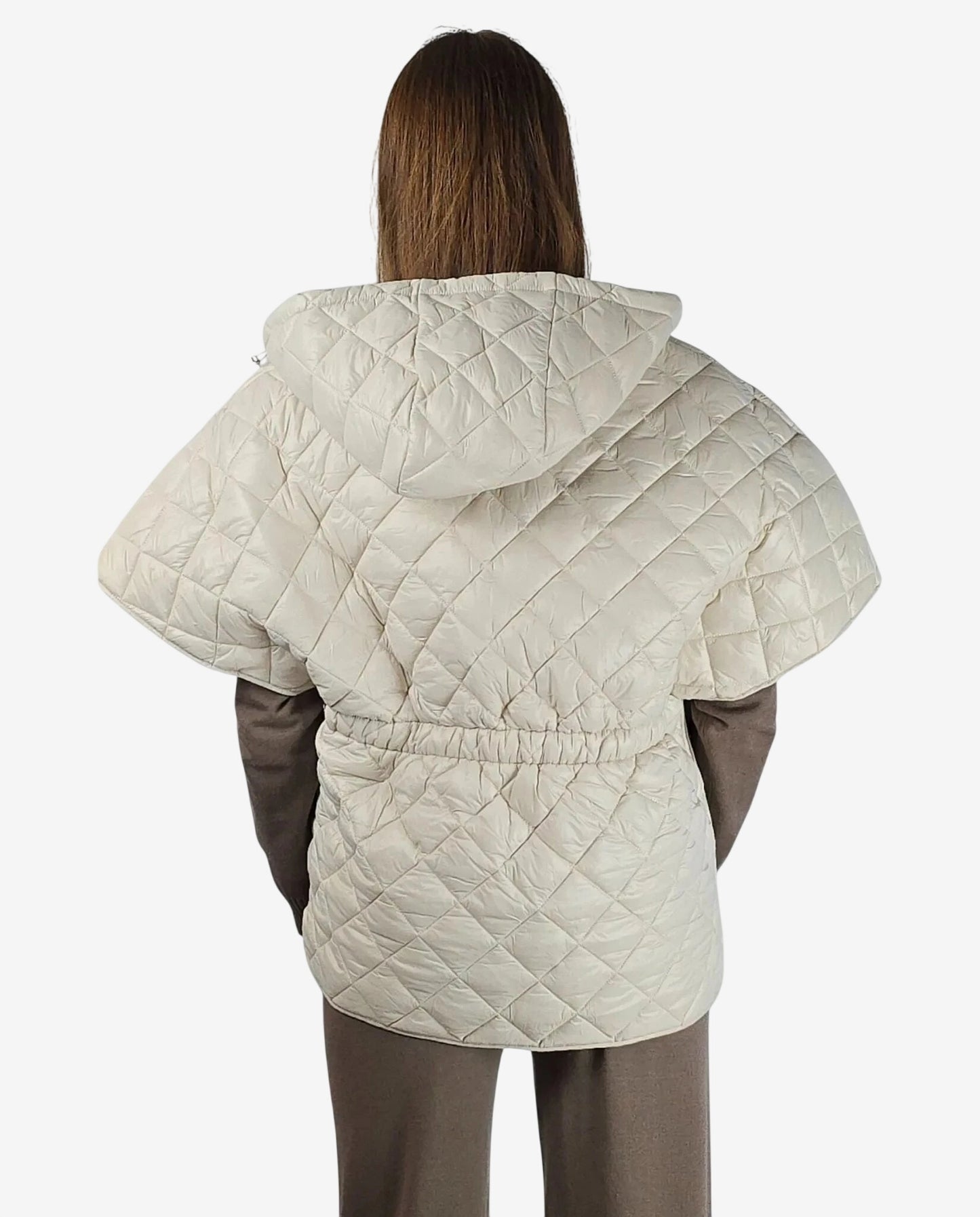 A person wears a cream-colored quilted hooded cape with a cinched waist over a brown outfit.
