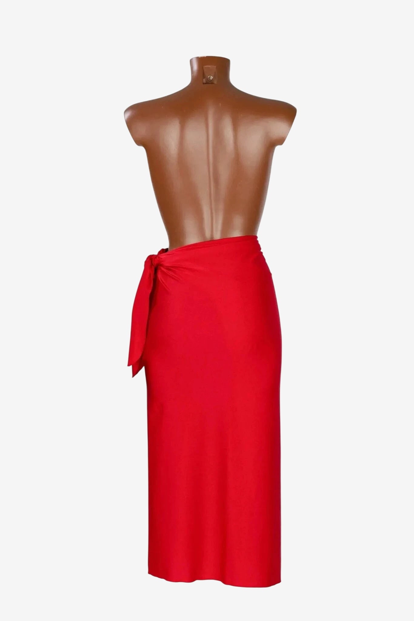 A red midi-length pareo skirt made of shiny lycra fabric tied at the side on a mannequin.