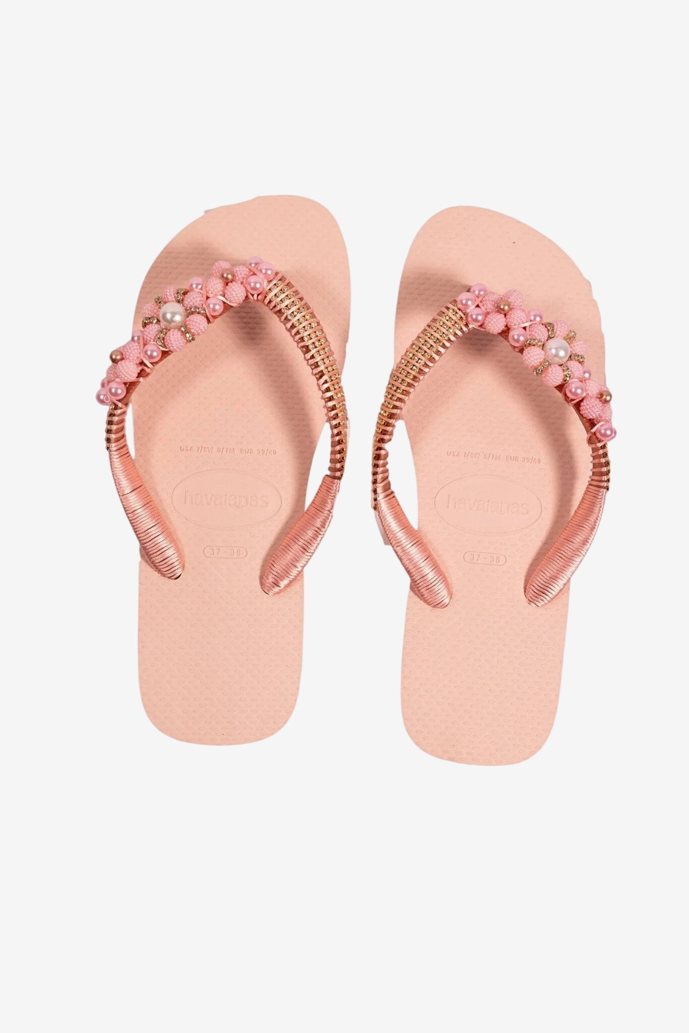 Infradito da donna color rosa con cinturini decorati da perline e dettagli metallici.