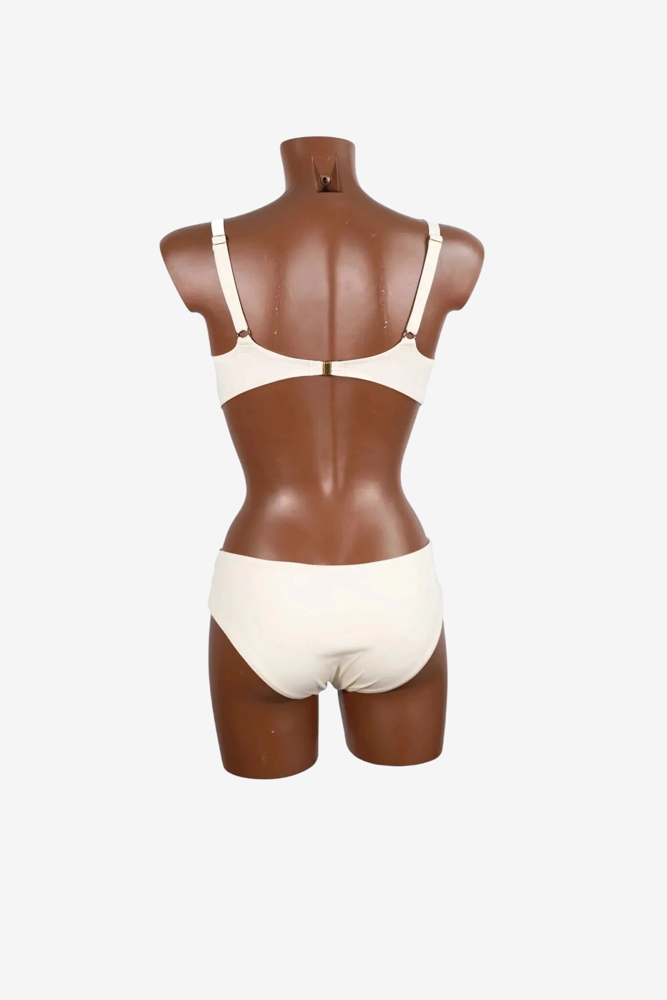 A white bralette and matching bikini bottom set displayed on a brown mannequin from the back.