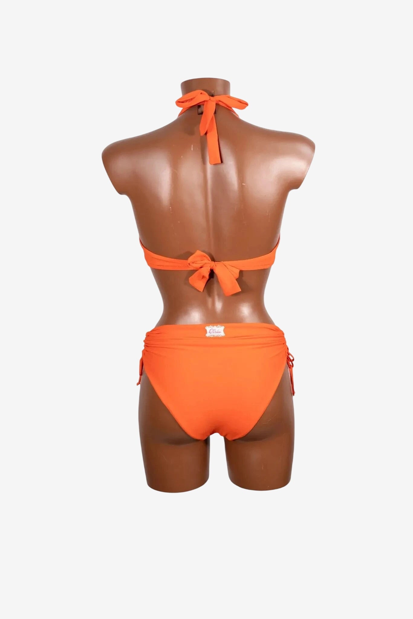 A bright orange bikini set with a tie-back top and ruched bottoms on a mannequin.