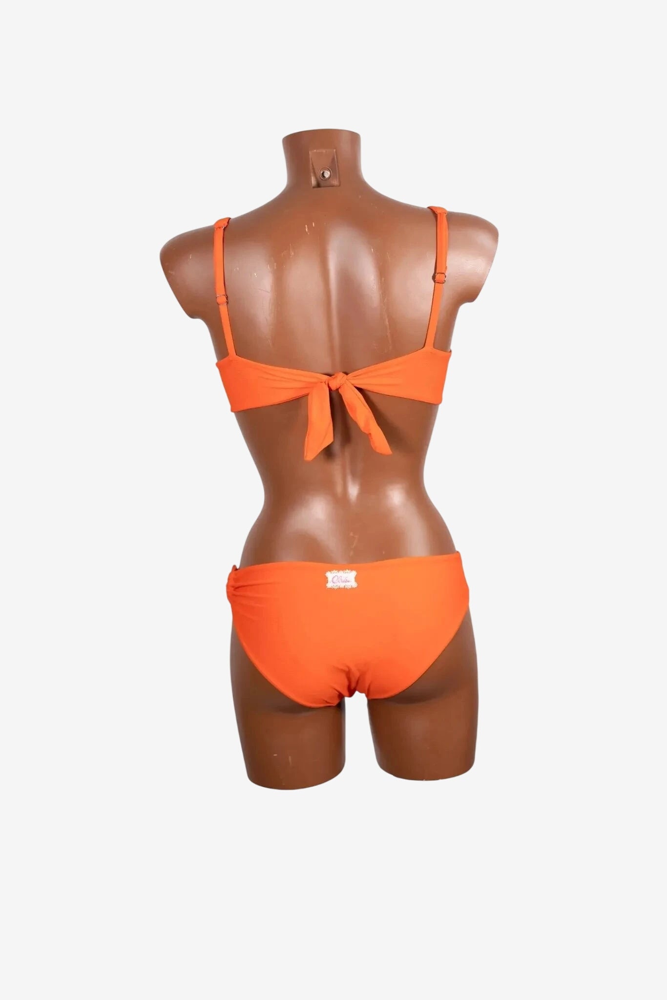A back view of a bright orange bikini set on a mannequin featuring a tie-back top and matching bottoms.
