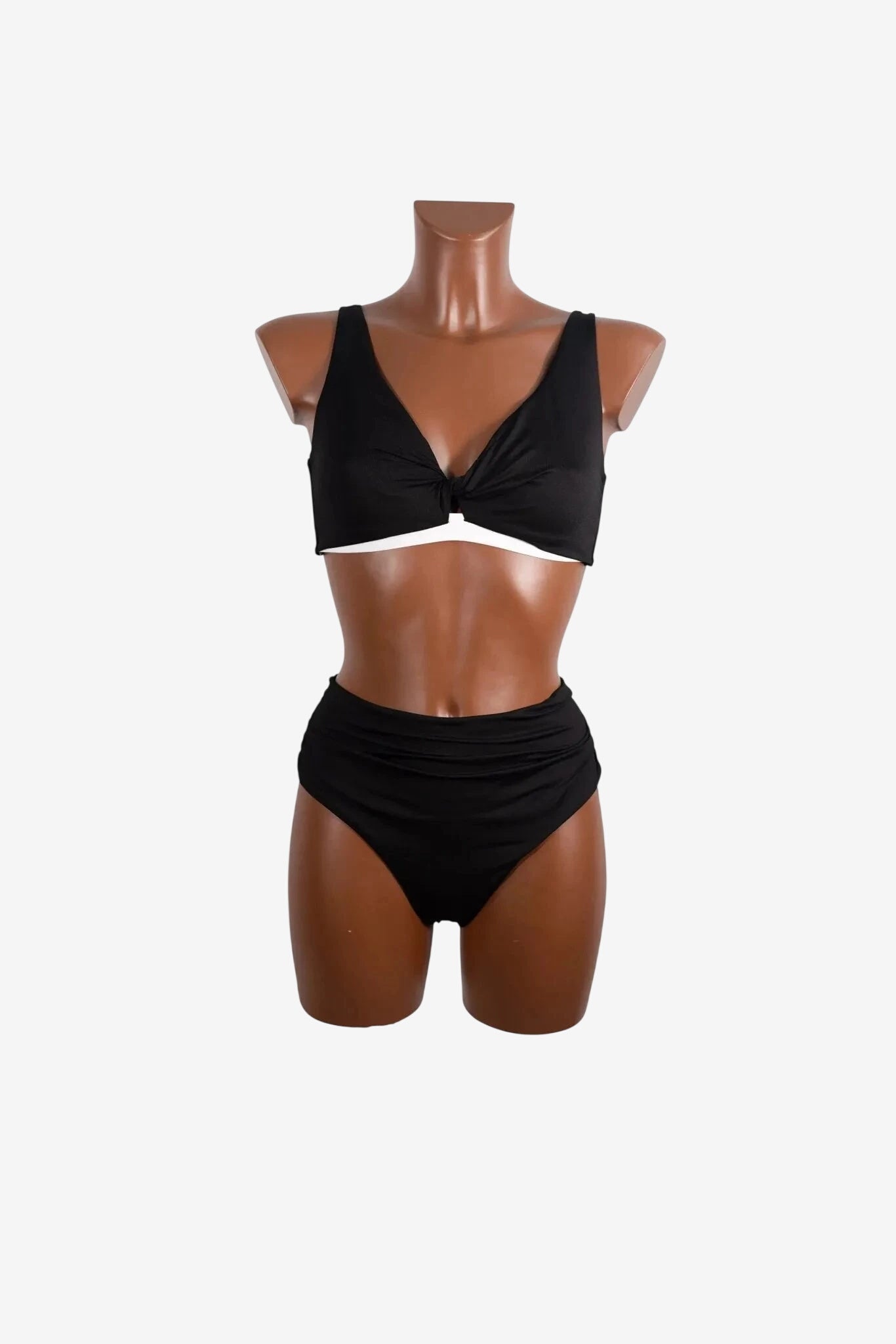 Bikini nero a due pezzi con top a V annodato e slip a vita alta arricciato su manichino.