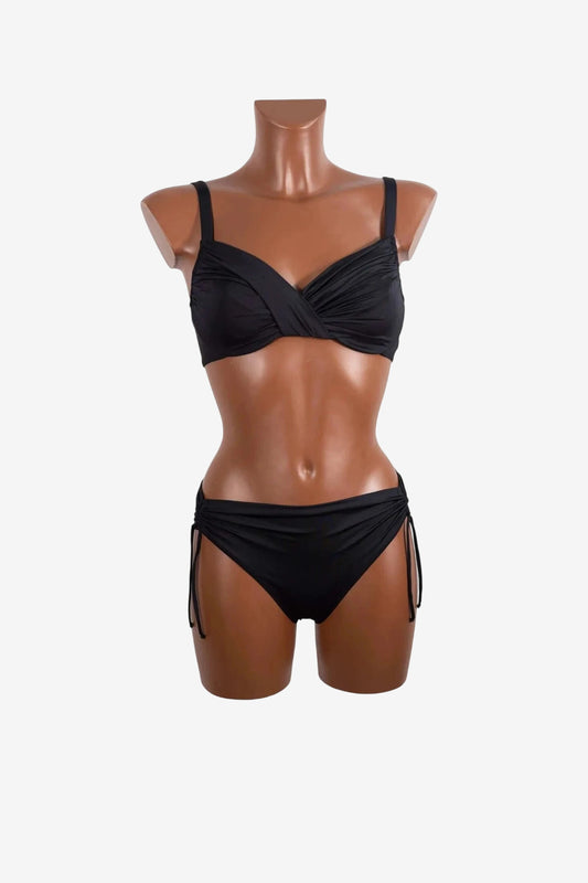 A black two-piece bikini with a ruched, cross-front top and side-tie bottoms on a mannequin.