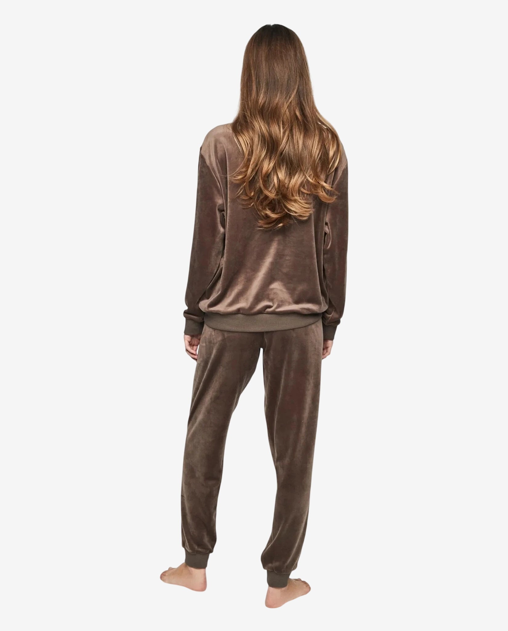 Donna di spalle indossa una tuta in ciniglia color tortora composta da felpa e pantaloni.