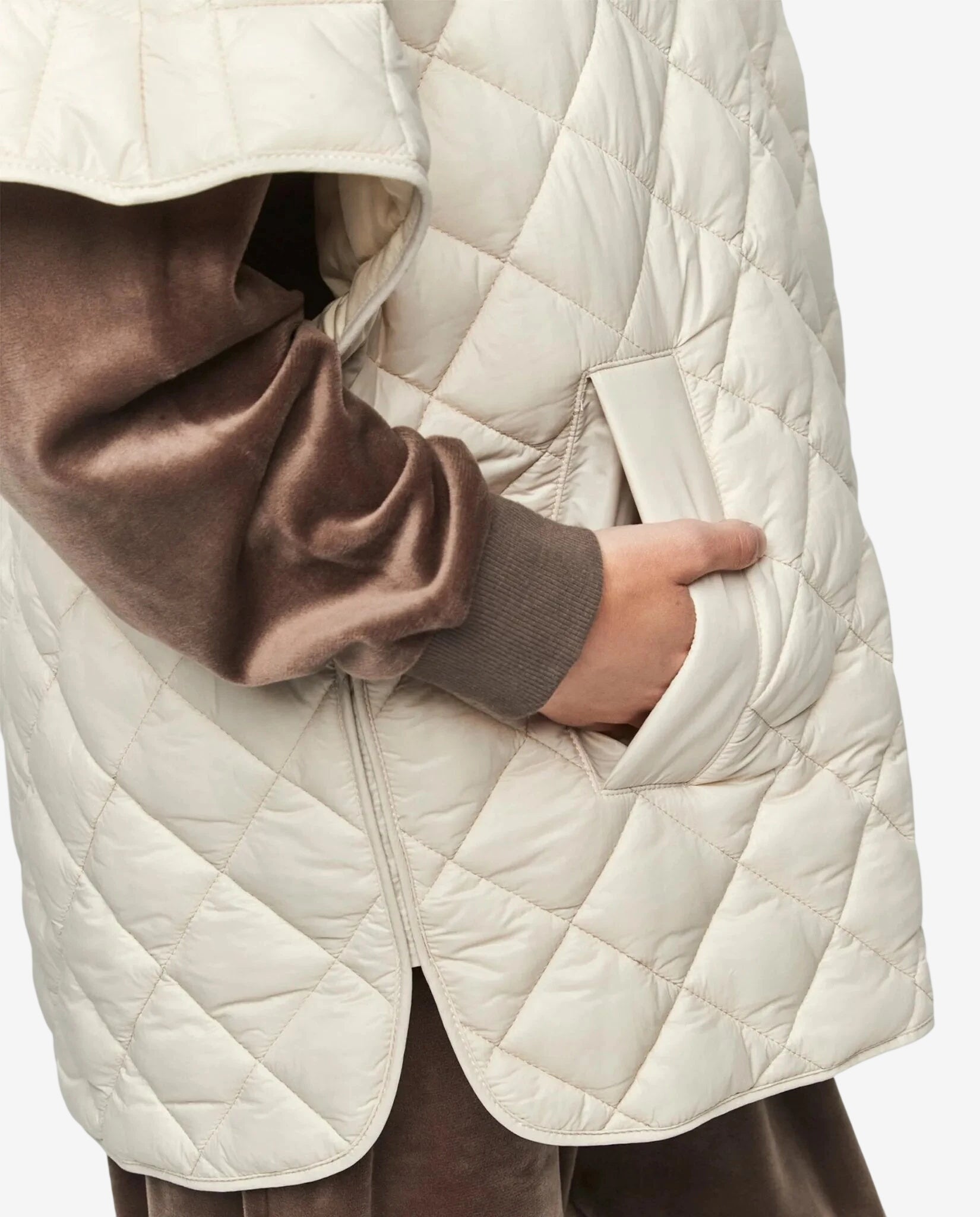 A person wears a cream-colored quilted vest over a brown velvet long-sleeved top.