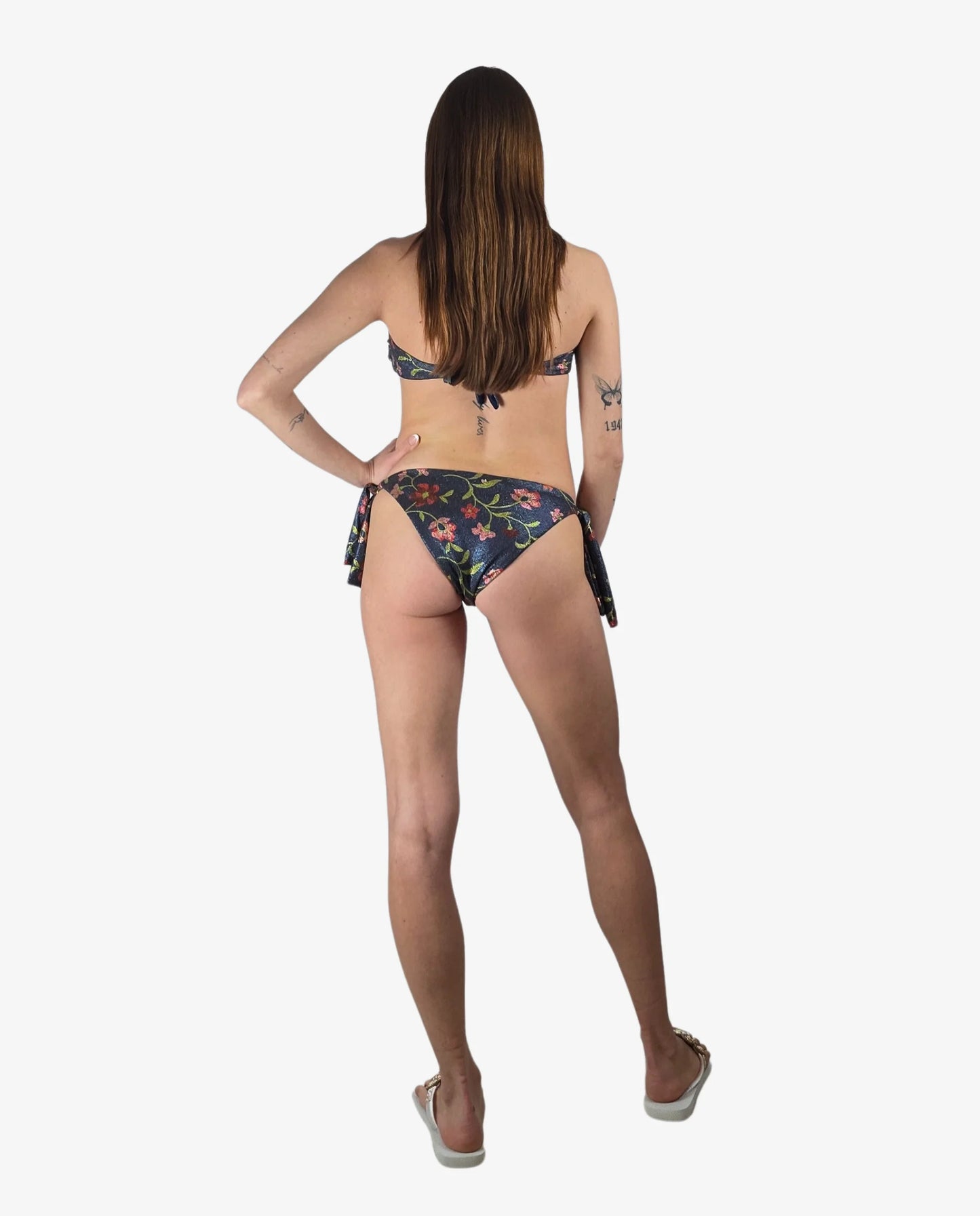 Modella di spalle indossa un bikini a fascia blu con fantasia floreale e dettagli lurex.