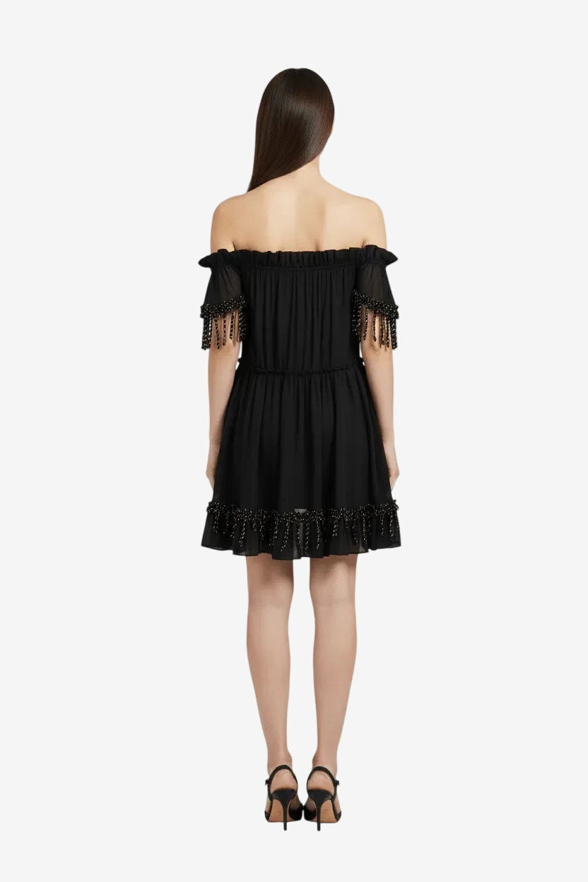 A short black off-the-shoulder dress with gold lurex fringe details on the sleeves and hem.