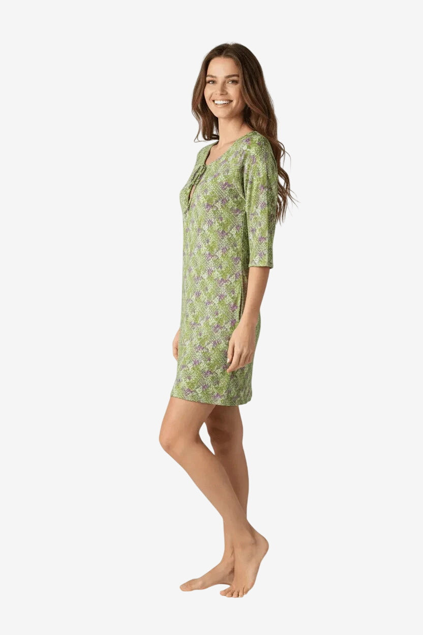 Una donna indossa un abito corto verde con stampa floreale viola e maniche a tre quarti.