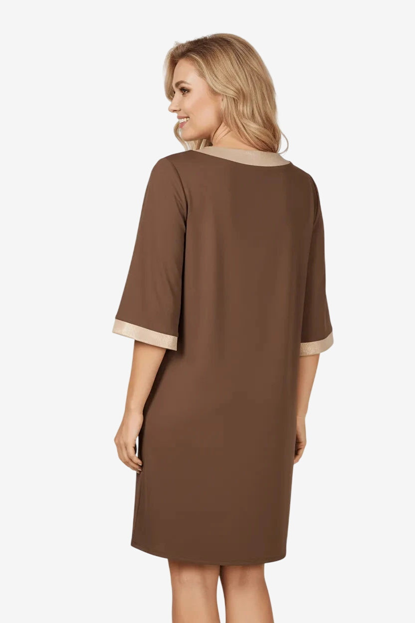 Una donna indossa un abito corto marrone con dettagli color oro su scollo e maniche.