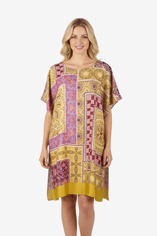 Donna che indossa un caftano corto con stampa patchwork multicolore su fondo giallo senape.