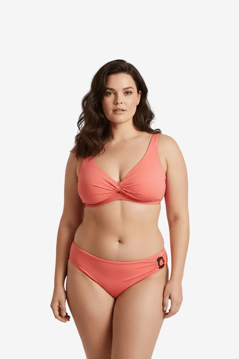 Modella indossa un bikini color corallo con reggiseno a fascia incrociata e slip con dettaglio.