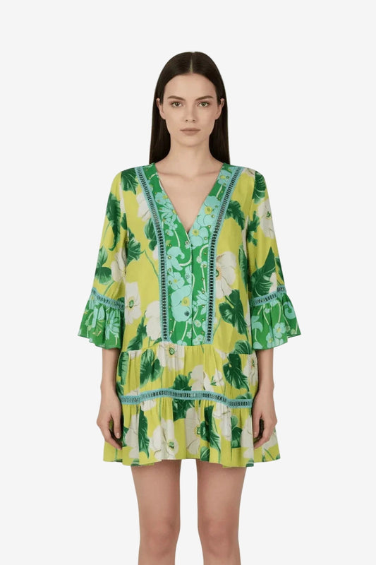 A model wears a short, lime green caftan dress featuring a vibrant floral print and lace trim.