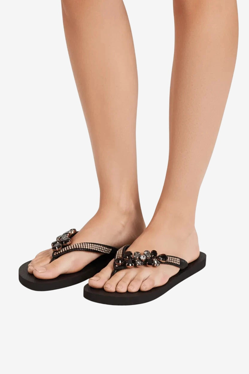 Infradito nere da donna con suola piatta e cinturini decorati da pietre scure e strass.