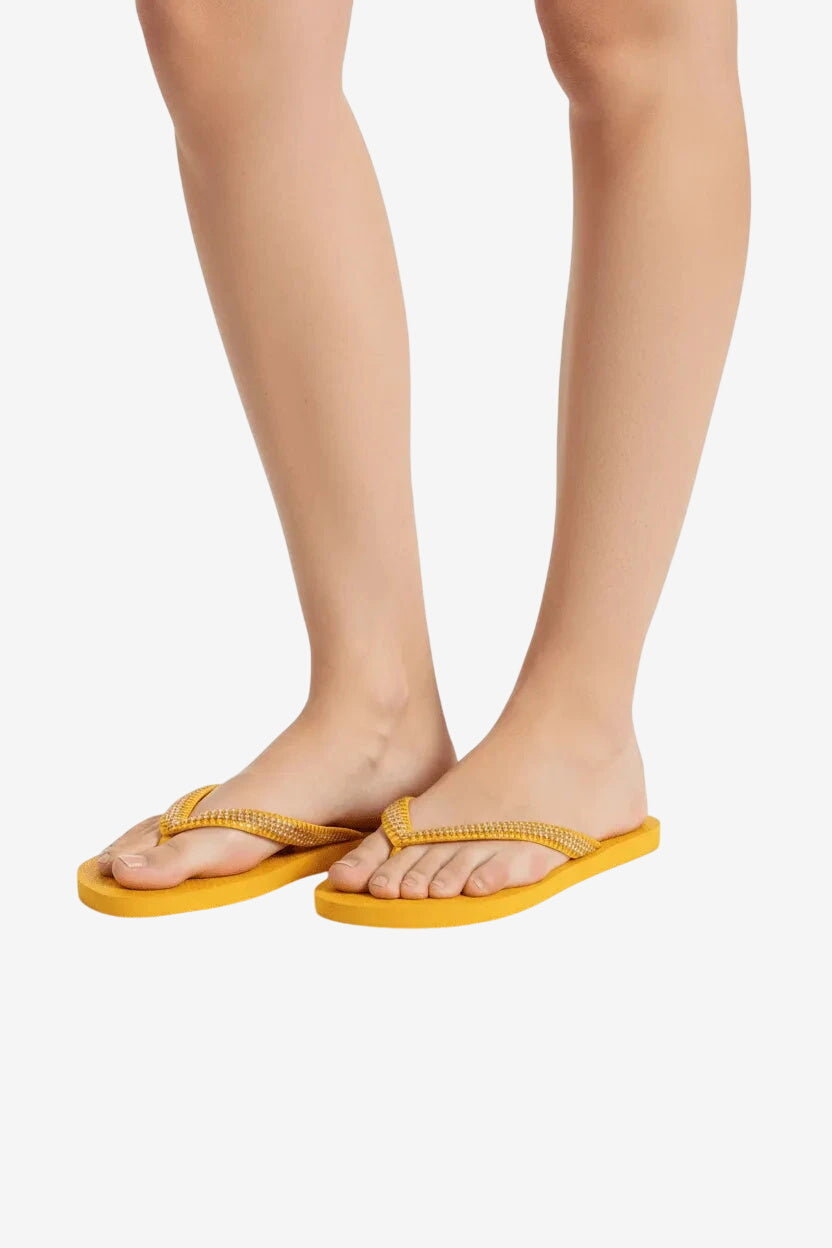 Infradito da donna color giallo sole con cinturini decorati indossate su sfondo bianco.