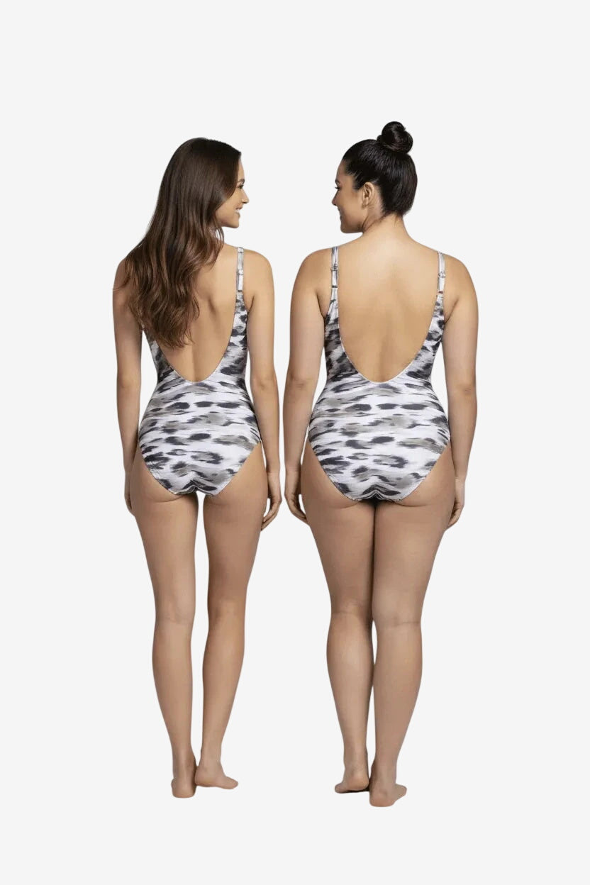 Two women stand back-to-back wearing matching black and white patterned one-piece swimsuits.