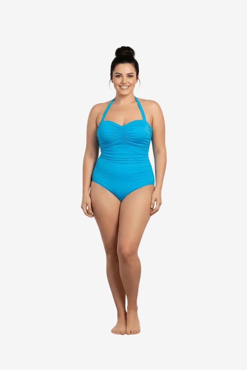 A woman wears a bright blue, ruched one-piece swimsuit with a halter neckline.