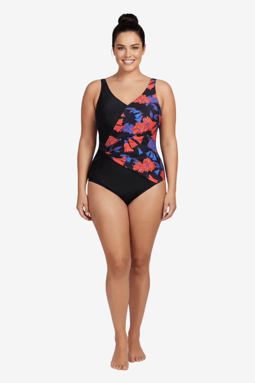 A woman wears a black one-piece swimsuit featuring a diagonal floral print panel and side ruching.