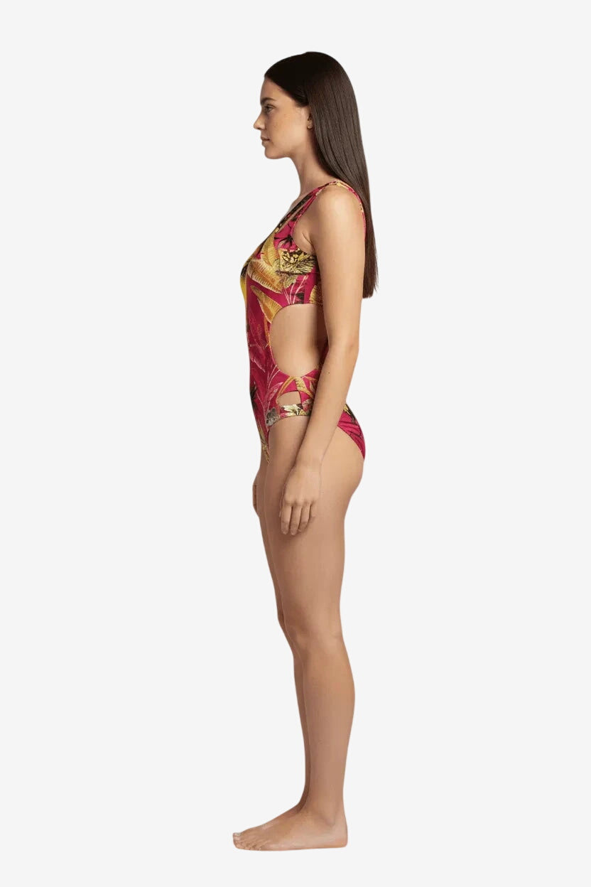 A woman wears a pink one-piece swimsuit with a tropical leaf print and side cutouts.
