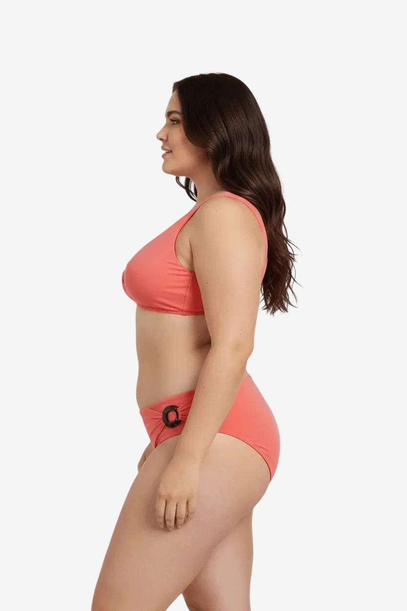 Modella di profilo indossa un bikini color corallo con dettaglio ad anello sul fianco.