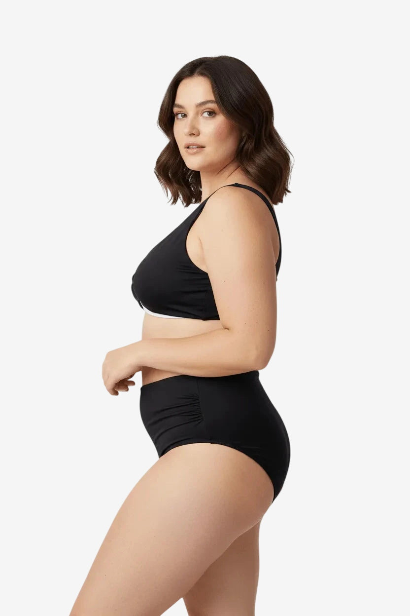 Modella di profilo indossa un bikini nero a vita alta con top a scollo a V e dettagli arricciati.