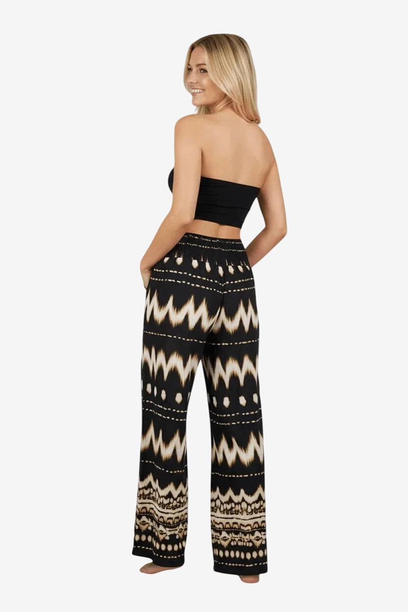 Una modella indossa pantaloni palazzo neri con una stampa etnica chiara e un top a fascia nero.