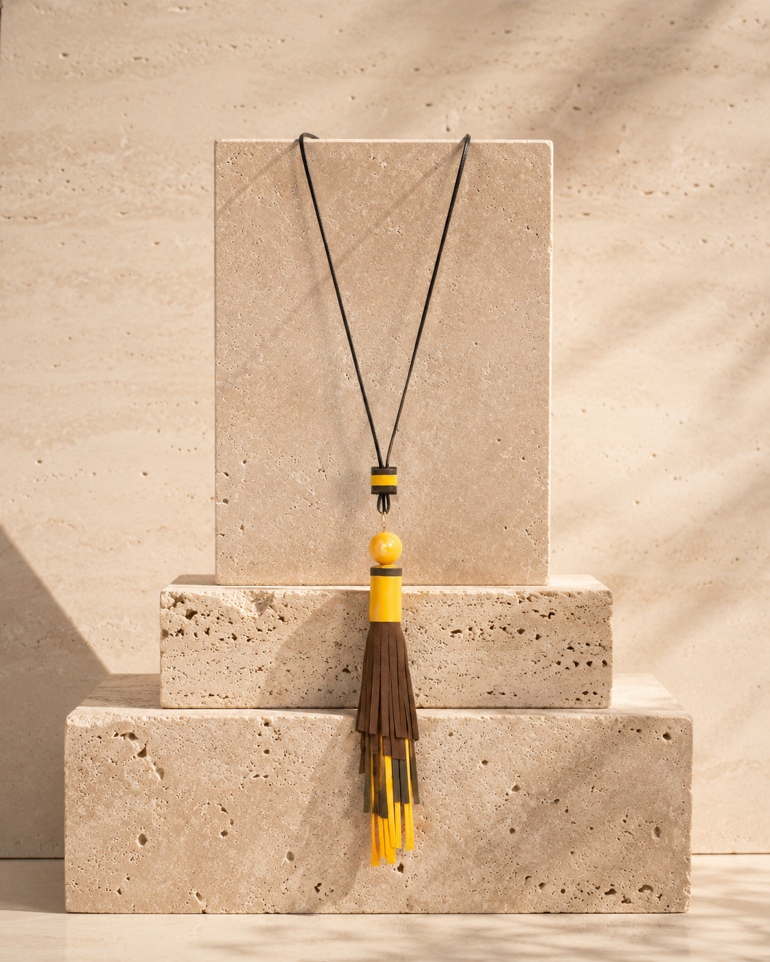 Collana artigianale con nappa in vera pelle colorata e perla in ceramica su cordoncino regolabile.