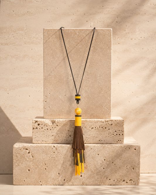 Collana artigianale con nappa in vera pelle colorata e perla in ceramica su cordoncino regolabile.
