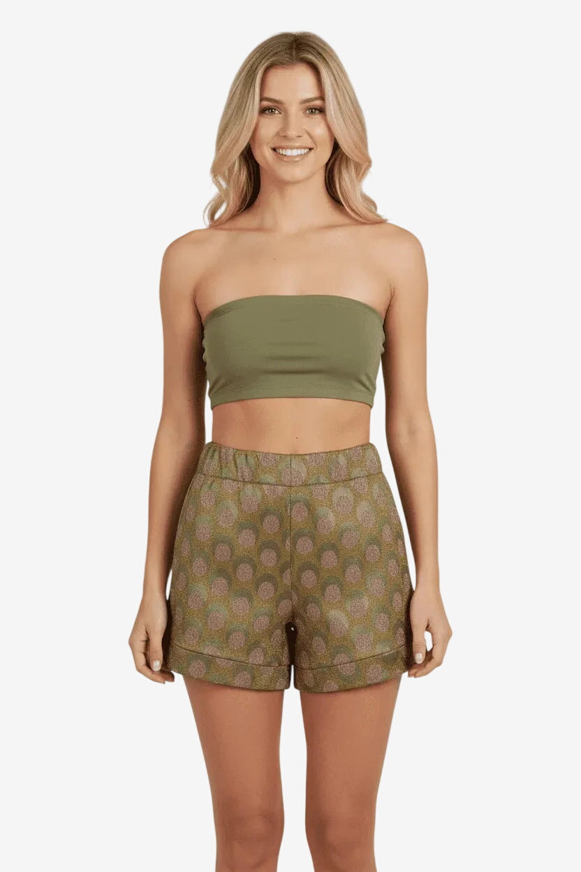 Modella indossa pantaloncini a vita alta con fantasia geometrica colorata su fondo verde.