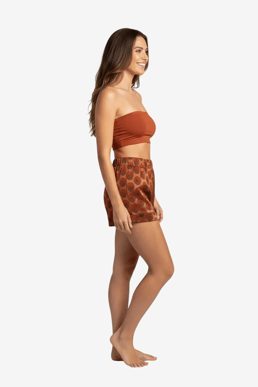 Modella di profilo indossa un pantaloncino corto color ruggine con fantasia a pois scuri.