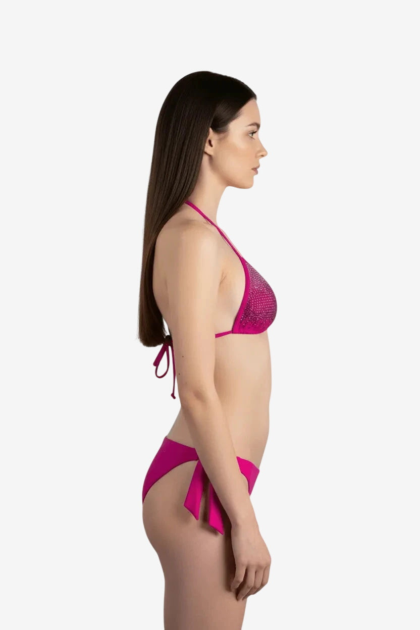 Modella di profilo indossa un bikini a triangolo fucsia decorato con strass luminosi.