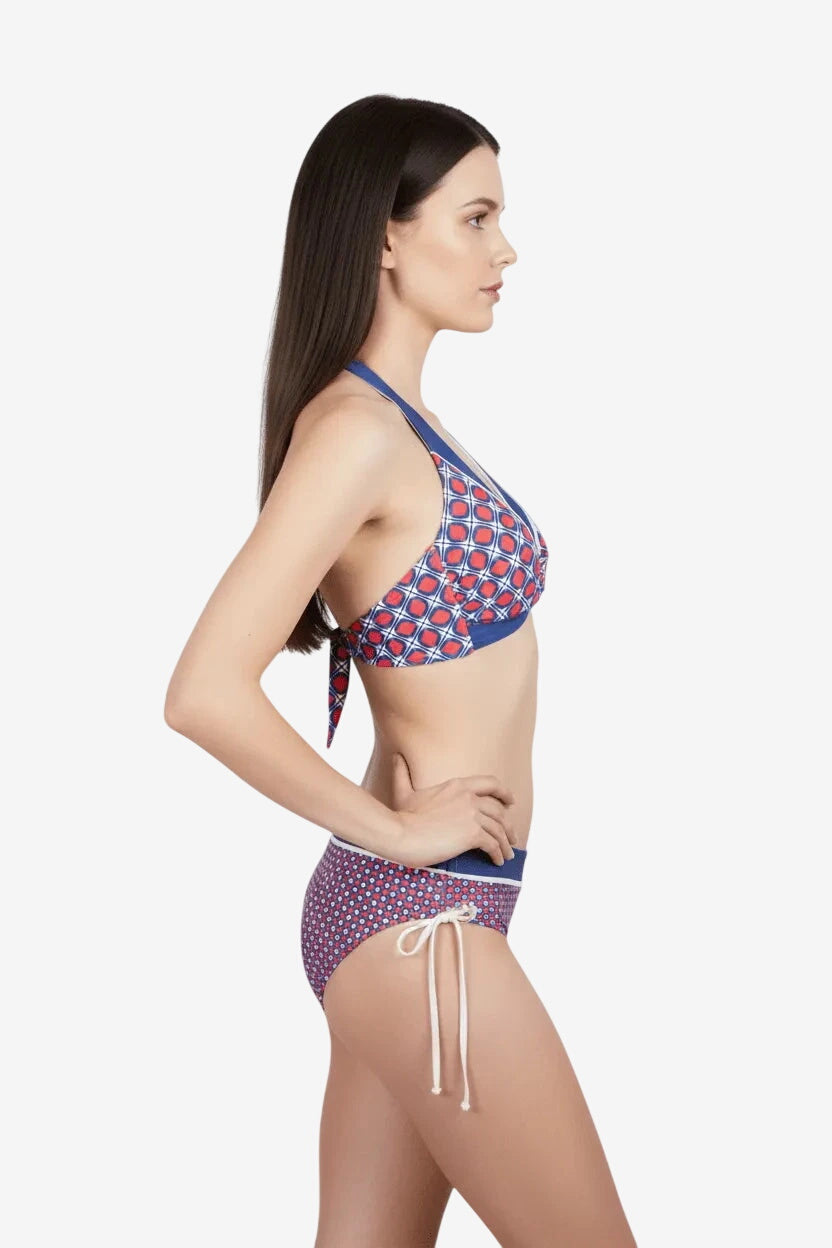 Modella di profilo che indossa un bikini triangolare con stampa geometrica rossa e blu.