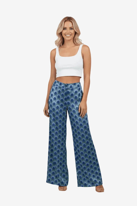 Modella indossa pantaloni a gamba larga con fantasia a pois blu e verdi su fondo azzurro.