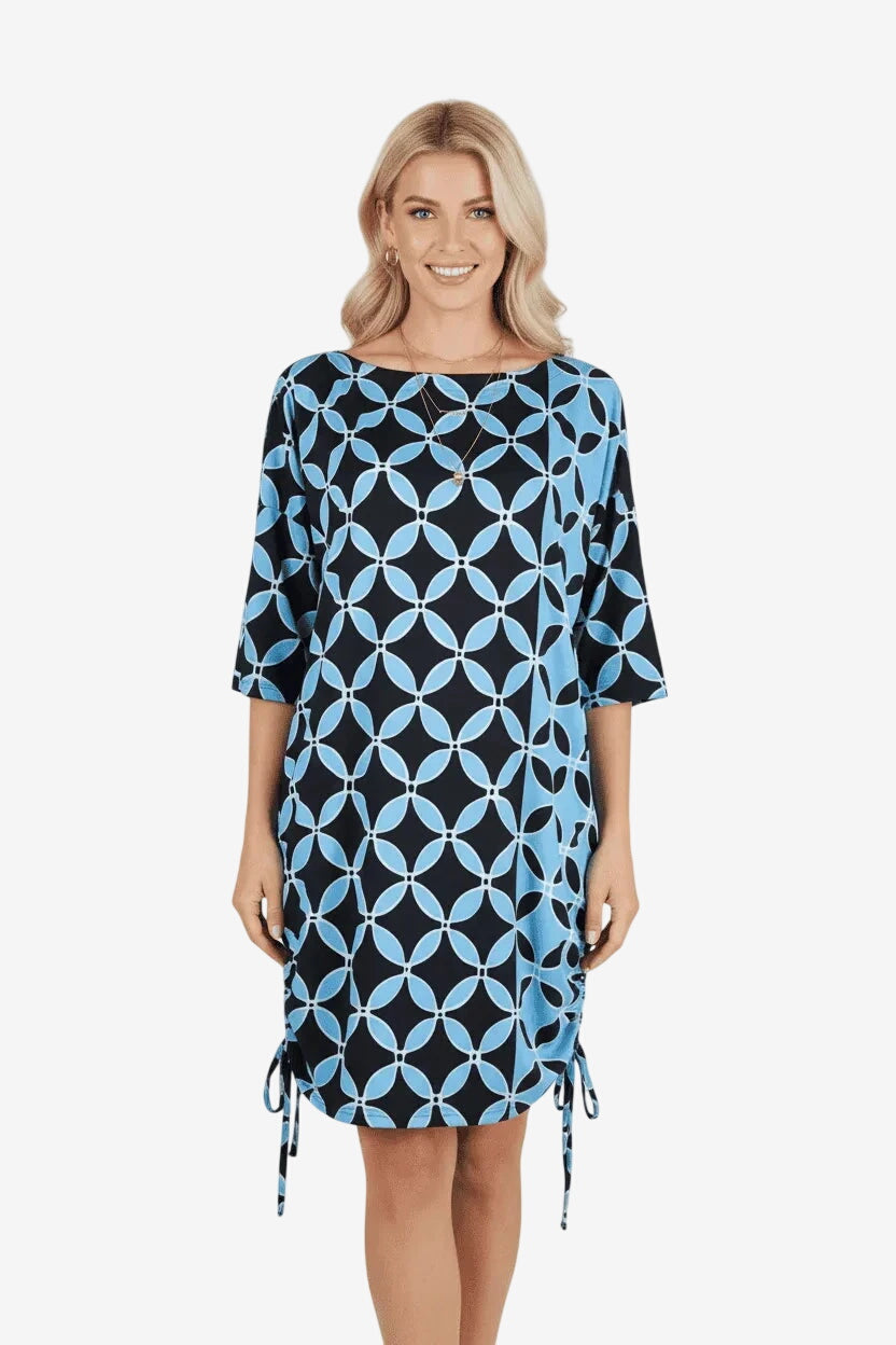 A woman wears a short, black and light blue geometric print dress with side drawstring details.