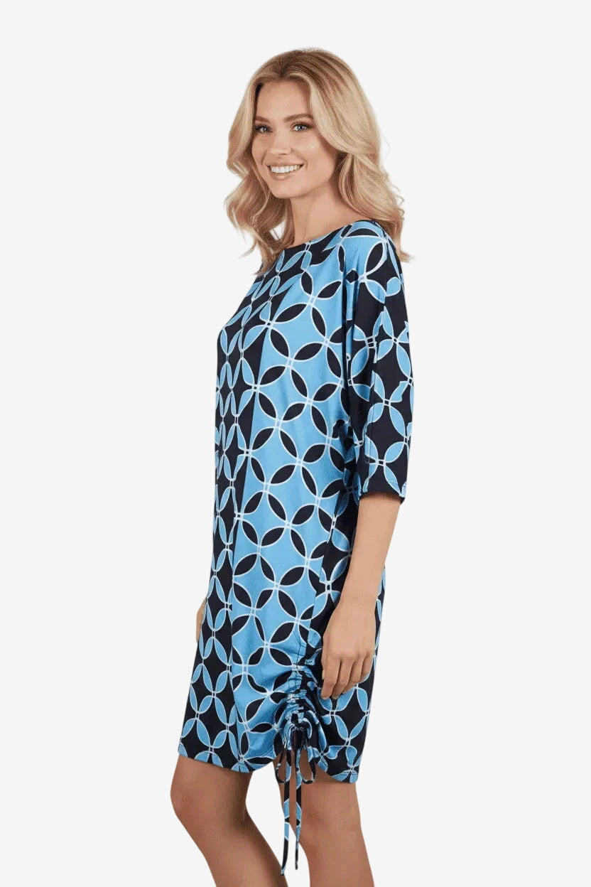A woman wears a short, blue and black geometric print dress with a drawstring side detail.